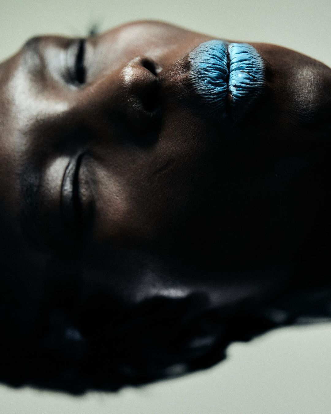 Dramatic beauty shot of a Black woman's face with blue lipstick in a studio, captured with a close-up, high-angle perspective.