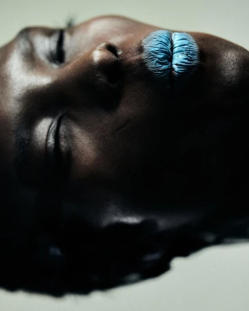 Dramatic beauty shot of a Black woman's face with blue lipstick in a studio, captured with a close-up, high-angle perspective.