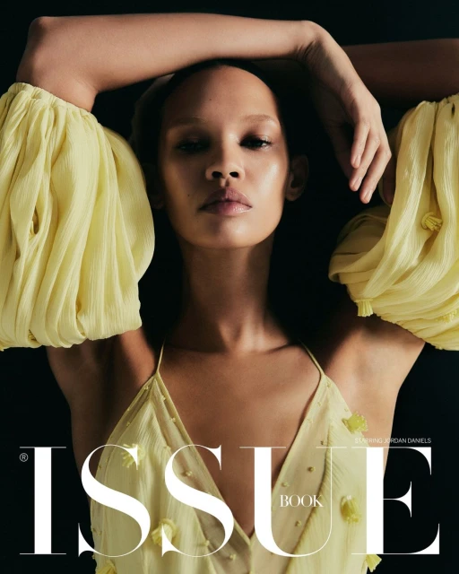 Fashion editorial shot of a Black woman with a yellow dress and puff sleeves against a black background. Magazine cover image.