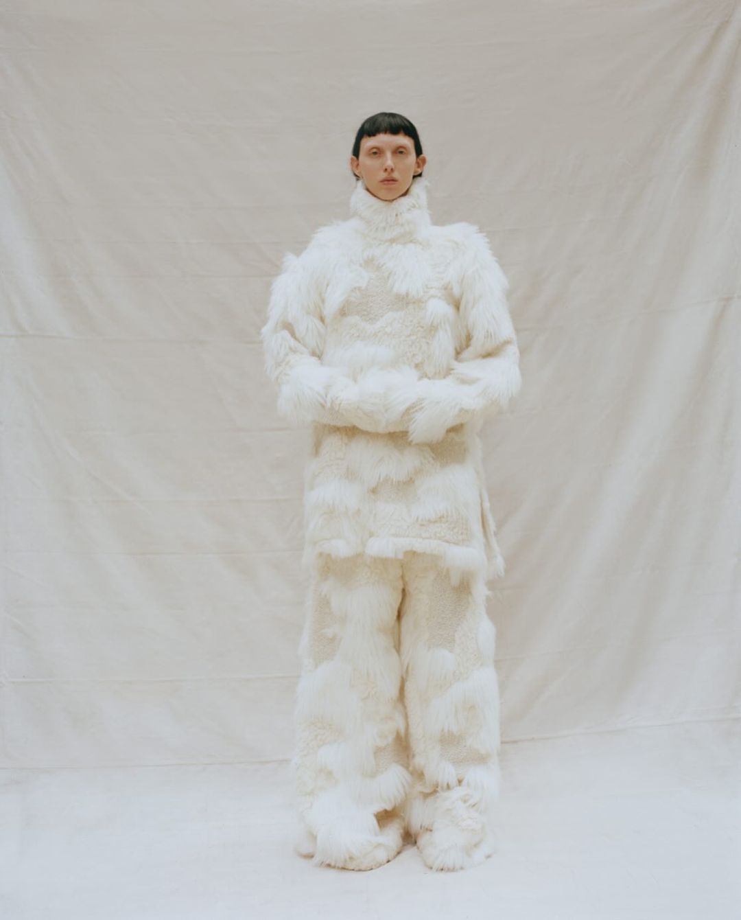 Full-length shot of a person wearing a fluffy white outfit, including a turtleneck top and wide-leg pants, standing in a studio setting.
