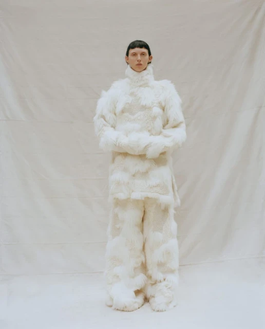 Full-length shot of a person wearing a fluffy white outfit, including a turtleneck top and wide-leg pants, standing in a studio setting.