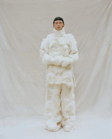 Full-length shot of a person wearing a fluffy white outfit, including a turtleneck top and wide-leg pants, standing in a studio setting.