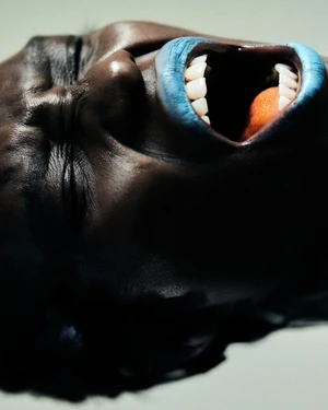 Extreme close-up portrait of a Black person with mouth wide open wearing bright blue lipstick against a light background