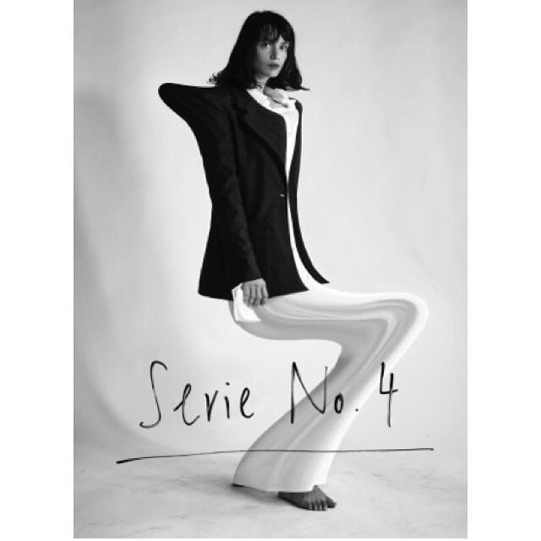 A woman in a black blazer and white pants poses in a studio with Serie No. 4 written at the bottom in black and white.