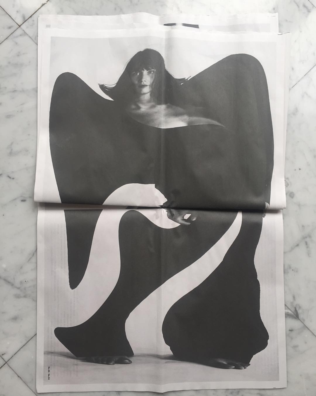 Black and white photograph of an adult female model in a newspaper, featuring dramatic, high-contrast visuals and minimal composition.