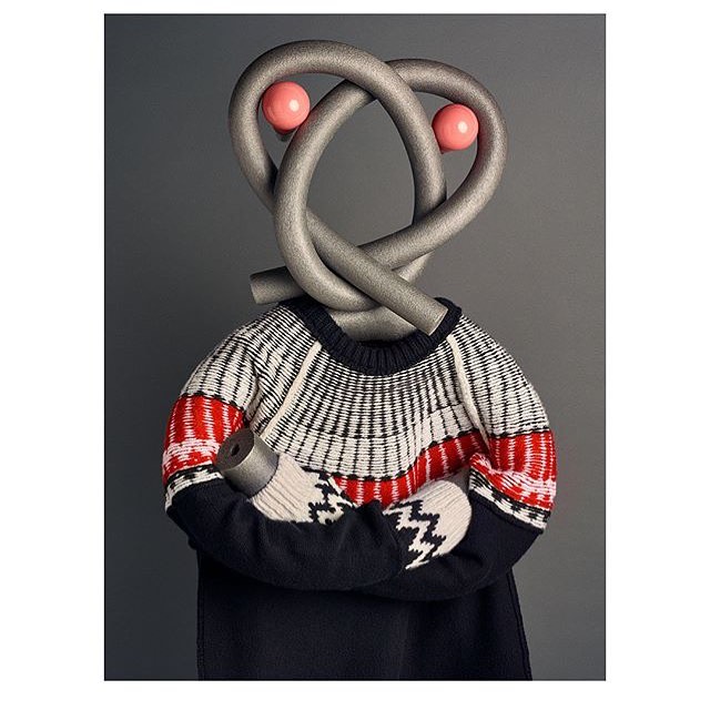 Whimsical studio shot of a sweater displayed on a torso form, topped with a playfully knotted gray pool noodle and pink spheres for eyes.