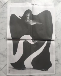 Black and white editorial print laid flat on a white marble surface featuring a woman in sculptural apparel.