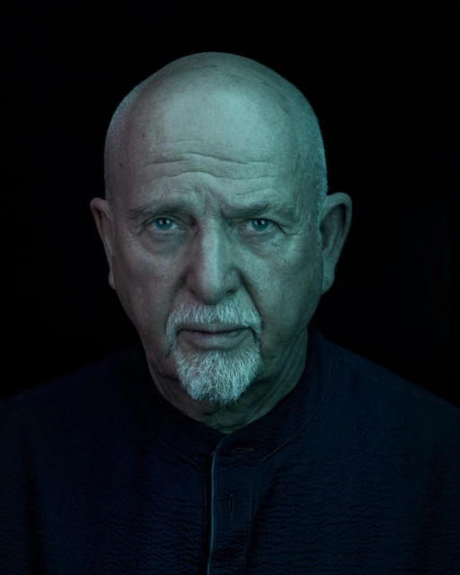Portrait of a mature man with a bald head and a goatee wearing a dark shirt in front of a dark background with rim lighting.