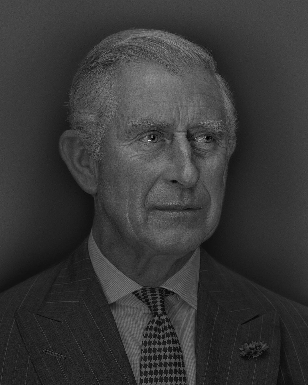 Monochrome portrait of adult male in pinstripe suit and patterned tie against dark background in eye-level shot.