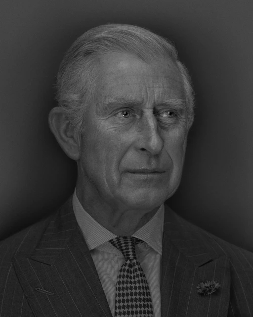 Monochrome portrait of adult male in pinstripe suit and patterned tie against dark background in eye-level shot.