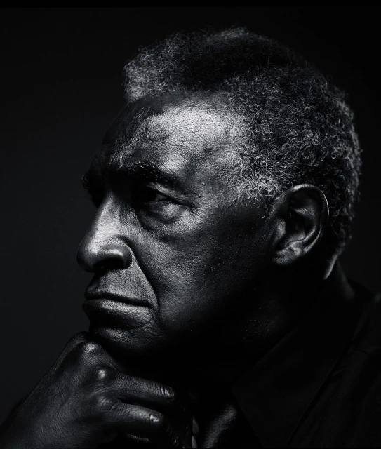 Monochrome portrait of African American man with hand on chin, shot in studio with dark background and soft lighting.