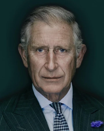 Headshot of an adult male with gray hair wearing a pinstripe suit, light blue shirt, and a patterned tie against a dark teal background.