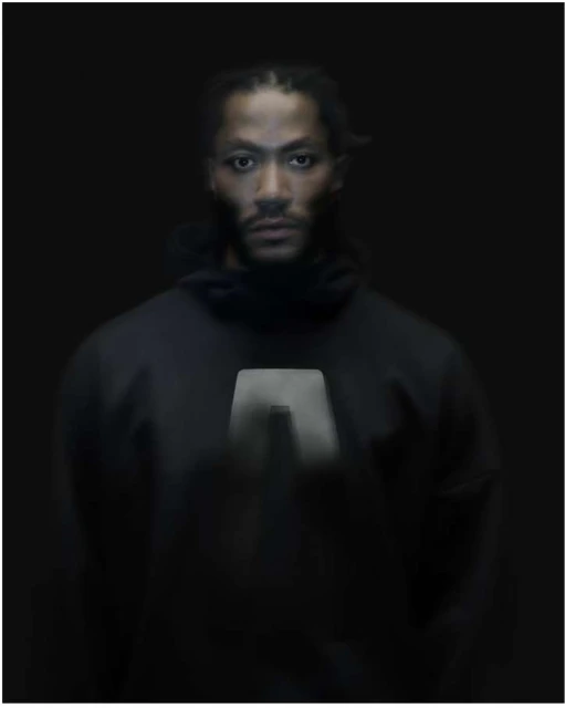 Portrait of African American adult male in dark hooded top against dark background. Intense gaze, studio lighting, and braids visible.