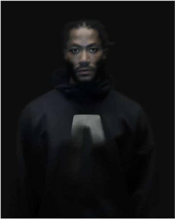 Portrait of African American adult male in dark hooded top against dark background. Intense gaze, studio lighting, and braids visible.
