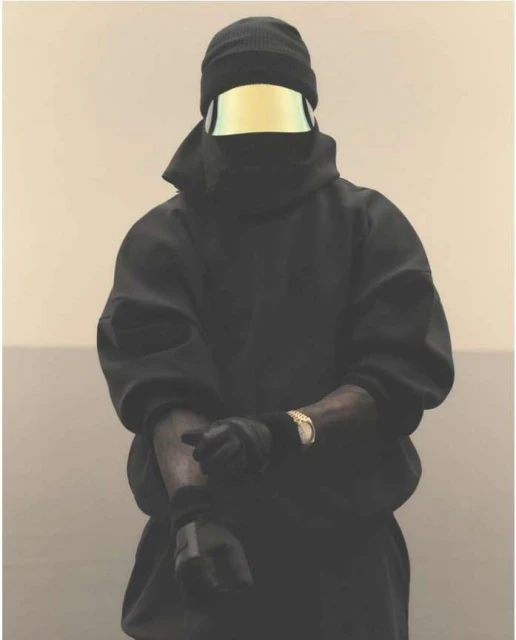 Adult male wearing a black beanie and an iridescent face shield, posing in a black hooded sweatshirt and gloves, with a gold watch.