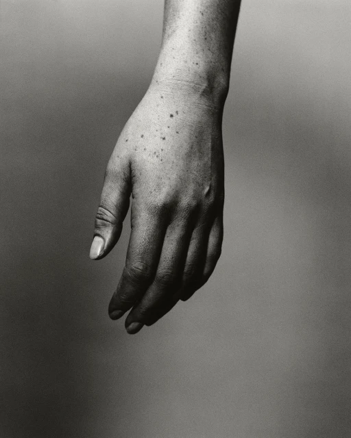 Monochromatic photograph of a light-skinned adult hand with freckles and visible veins against a neutral gray backdrop.