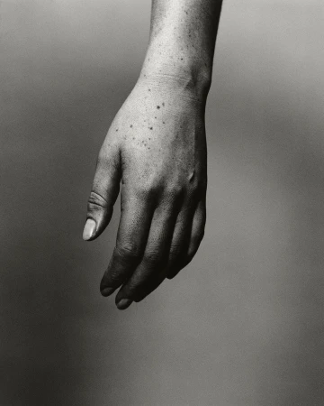 Monochromatic photograph of a light-skinned adult hand with freckles and visible veins against a neutral gray backdrop.