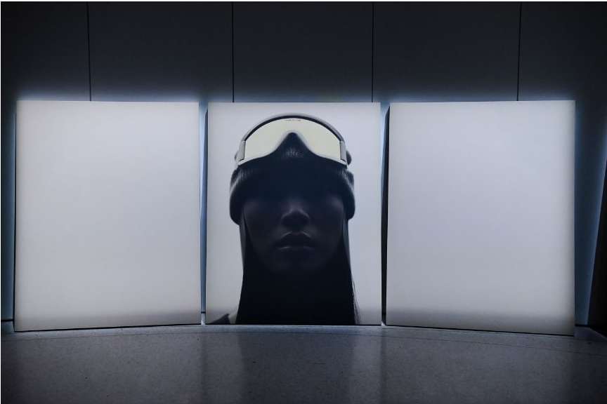 Portrait of a woman in a beanie and ski goggles against three vertically stacked white panels in a dimly lit indoor setting.