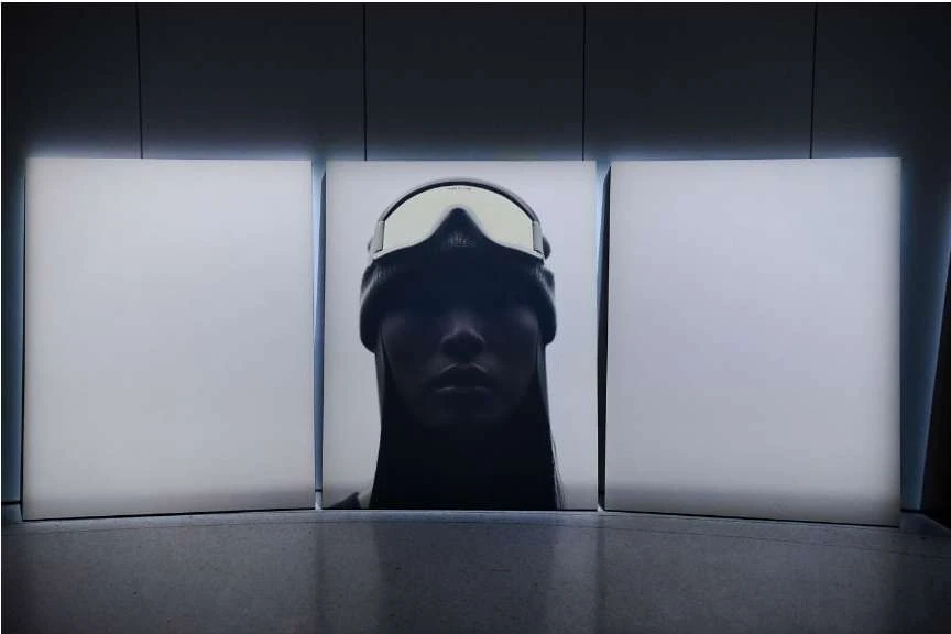 Portrait of a woman in a beanie and ski goggles against three vertically stacked white panels in a dimly lit indoor setting.