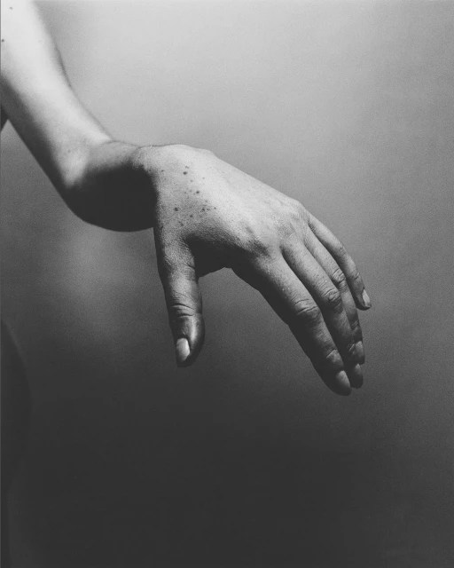 Monochrome studio shot of a person's forearm and hand, palm facing down, on a plain gray backdrop, emphasizes texture and form.