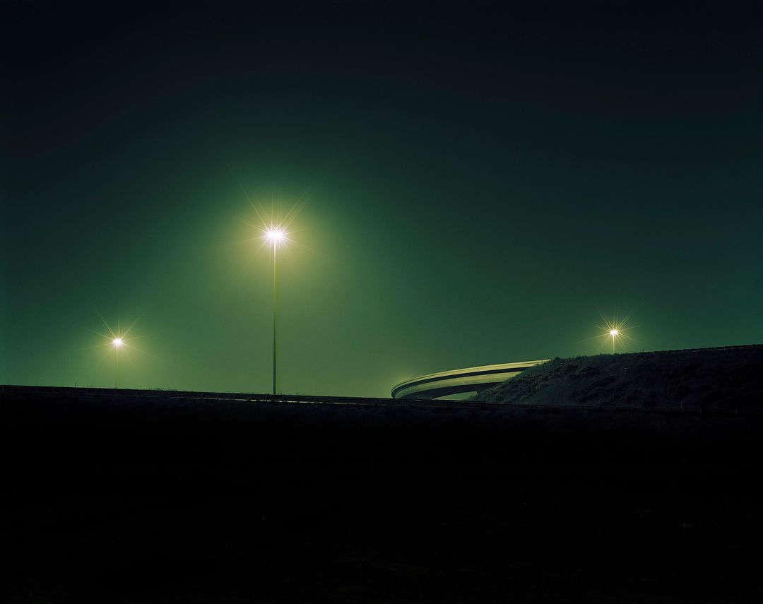 Three streetlights illuminate a dark road and a building in the background, creating a moody and atmospheric scene at night.