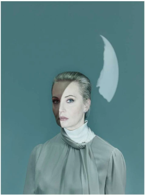 Woman portrait with half her face shadowed and a light projection on a solid background, wearing a blouse and turtleneck.