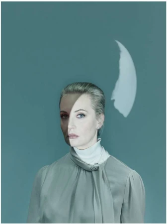 Woman portrait with half her face shadowed and a light projection on a solid background, wearing a blouse and turtleneck.