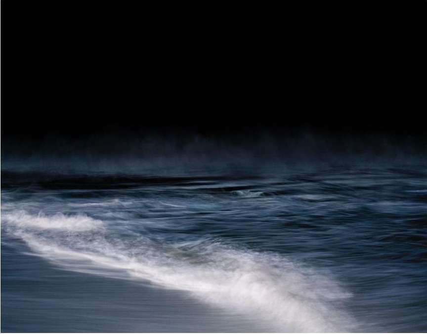 Seascape with dark sky over an ocean. Blue ocean waves move in a blur of motion. The water is a mix of navy and white.