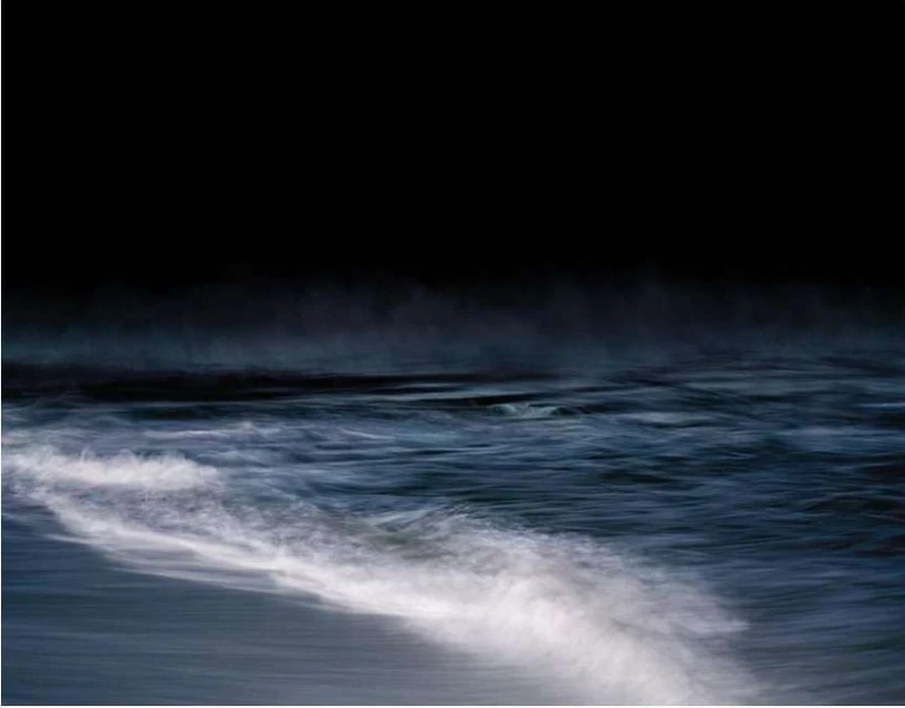 Seascape with dark sky over an ocean. Blue ocean waves move in a blur of motion. The water is a mix of navy and white.