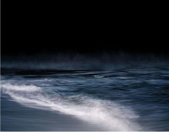 Seascape with dark sky over an ocean. Blue ocean waves move in a blur of motion. The water is a mix of navy and white.