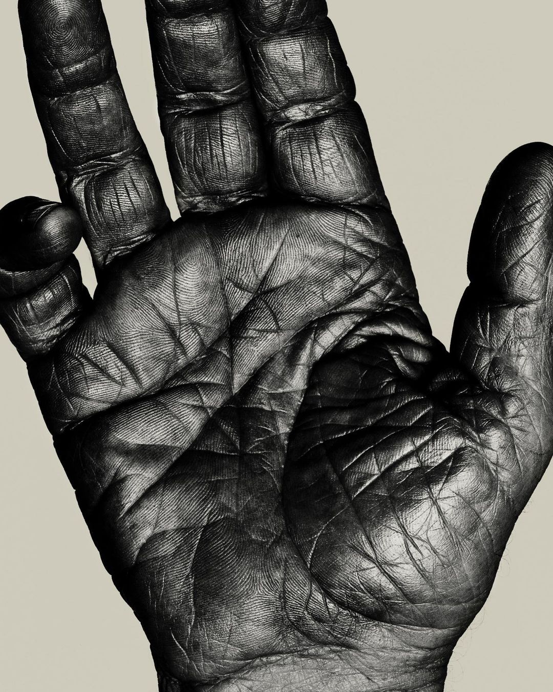 Close-up photograph of a dark-skinned human hand displaying detailed textures, lines, and ridges against a neutral background.