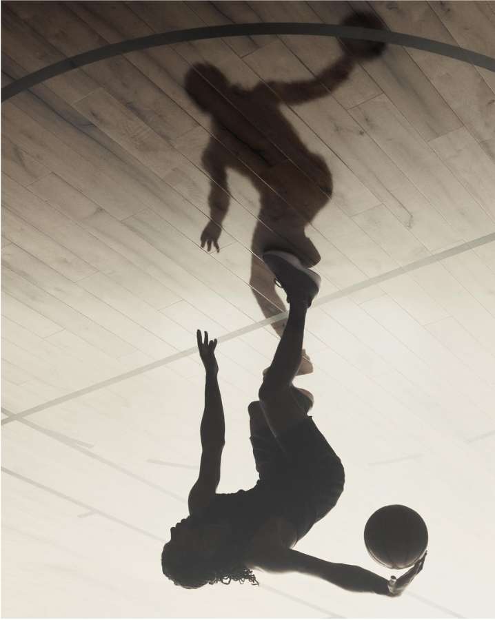 Silhouette of a woman playing basketball indoors with a shadow of a man on the wooden court, high contrast and motion captured.