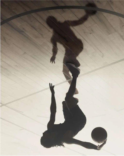 Silhouette of a woman playing basketball indoors with a shadow of a man on the wooden court, high contrast and motion captured.