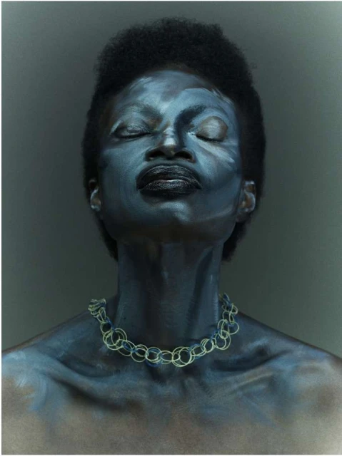Portrait of African American woman with closed eyes, face paint, and necklace against a dark grey background in a close-up shot.