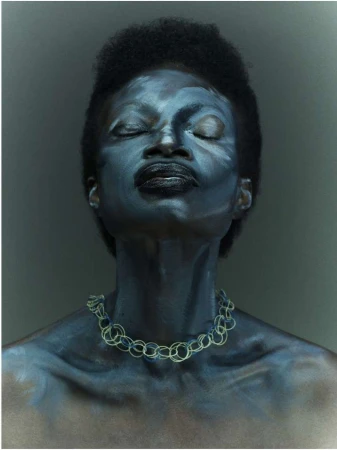 Portrait of African American woman with closed eyes, face paint, and necklace against a dark grey background in a close-up shot.