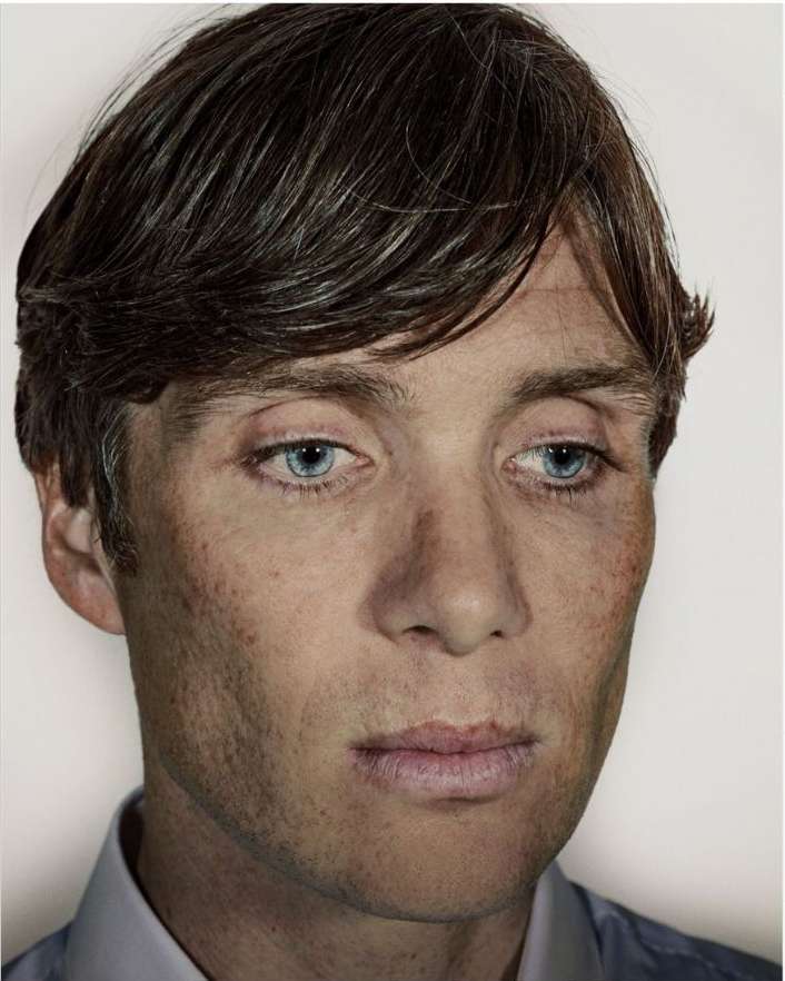 Close-up portrait of adult male with brown hair and blue eyes wearing a collared shirt against a white backdrop in a photo studio.