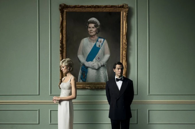 Portrait of a woman and a man standing in front of a large painting of a queen in a formal setting with green paneled walls.