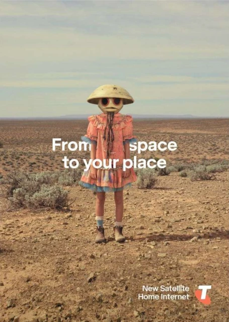 Child stands in a desert landscape wearing an unusual, round-faced mask and a vintage dress in a conceptual advertising image.