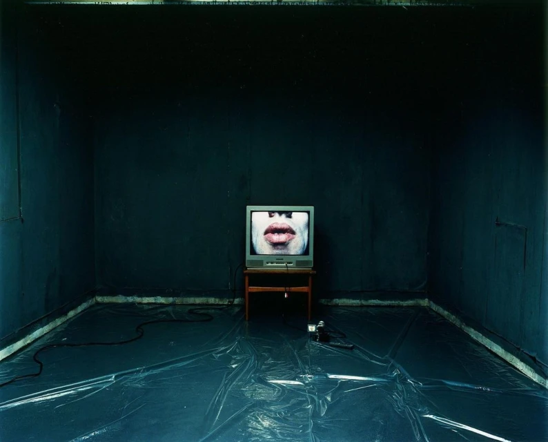 Old television displays a close-up of human lips and teeth, centered in a dark room with plastic sheeting on the floor.