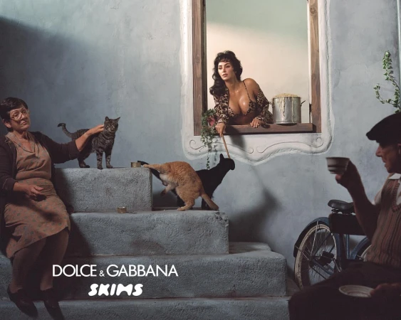Indoor fashion shot of a model looking out of a window, with cats on steps, an older woman, and an older man with a teacup.