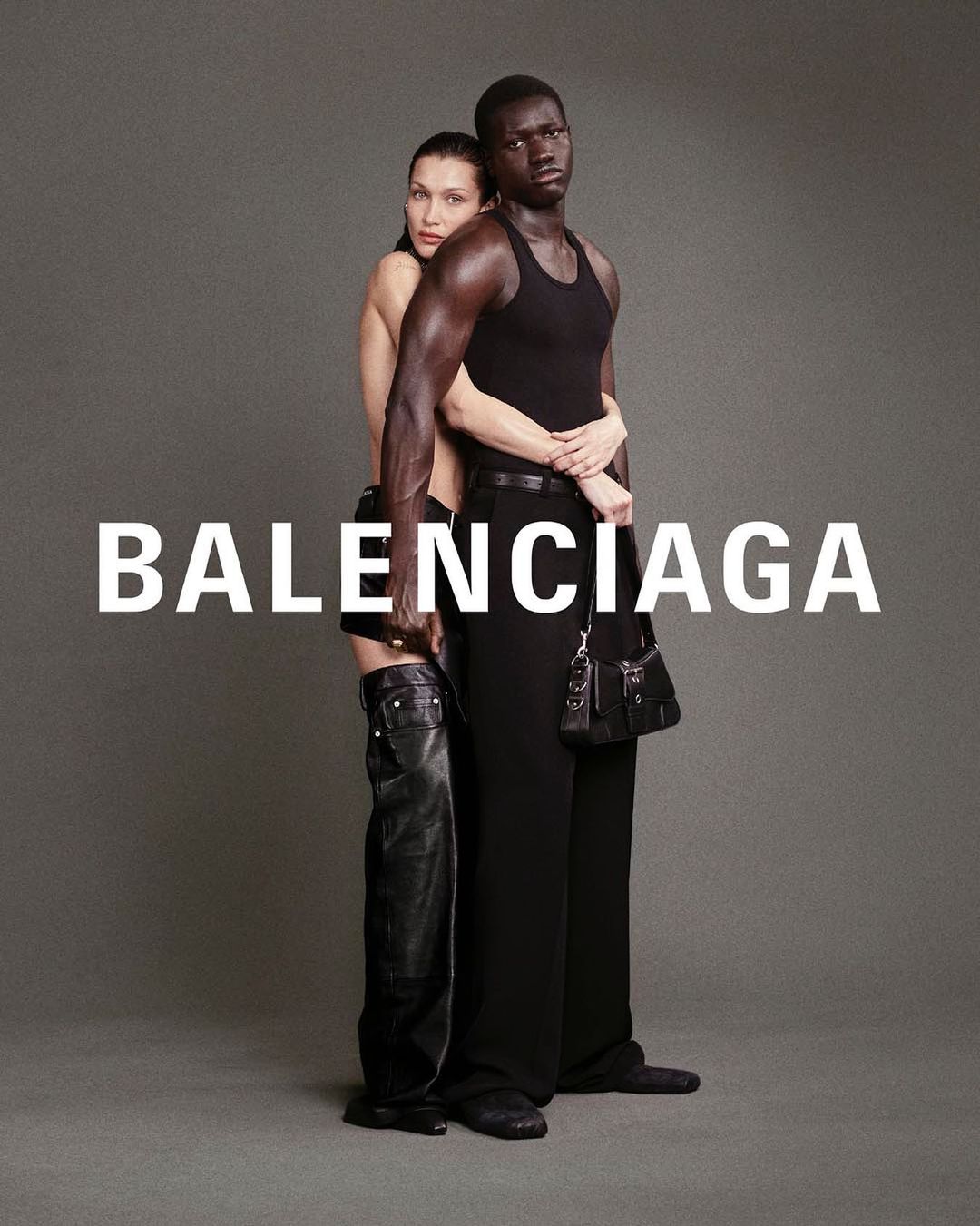 Two fashion models pose for Balenciaga, one in black tank top and trousers, the other in thigh-high leather boots and short trousers.