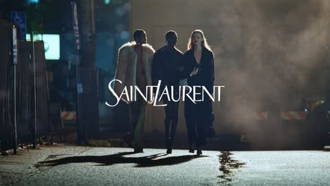 Three models walk down a dimly lit street in a Saint Laurent advertisement, showcasing fashion and urban style in a nighttime setting.