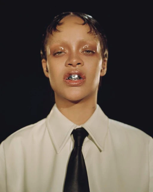 Close-up portrait of a woman with tan skin, wearing a white shirt and black tie, with a silver grill on her teeth, against a dark background.