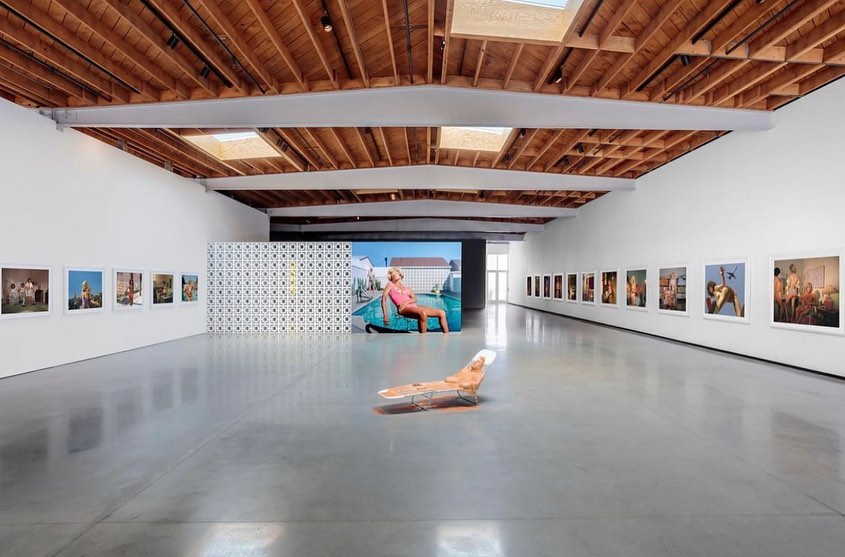 Art gallery exhibition space featuring photographic works with a central sculpture, set against a bright, minimalist interior.