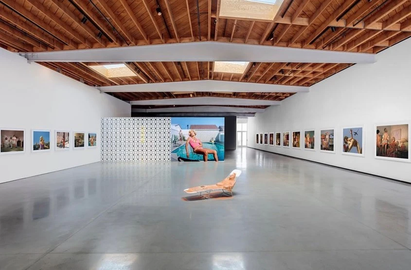 Art gallery exhibition space featuring photographic works with a central sculpture, set against a bright, minimalist interior.