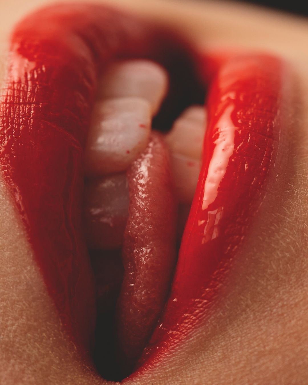Close-up shot of a person's mouth with bright red lipstick, revealing white teeth and the tip of their tongue.