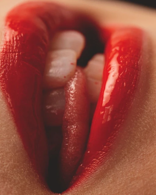 Close-up shot of a person's mouth with bright red lipstick, revealing white teeth and the tip of their tongue.