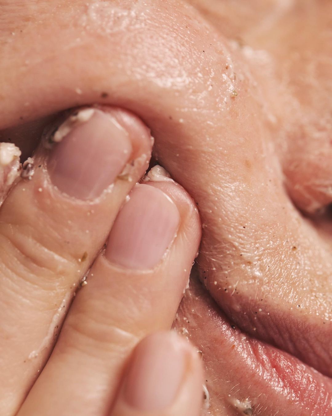 Close-up shot of person's face with finger rubbing exfoliating cream on the upper lip, showing skin texture and skincare routine.