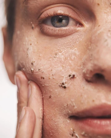Close-up of a fair-skinned person's face with a cosmetic scrub applied, hand gently touching the face. Skincare and beauty concept.