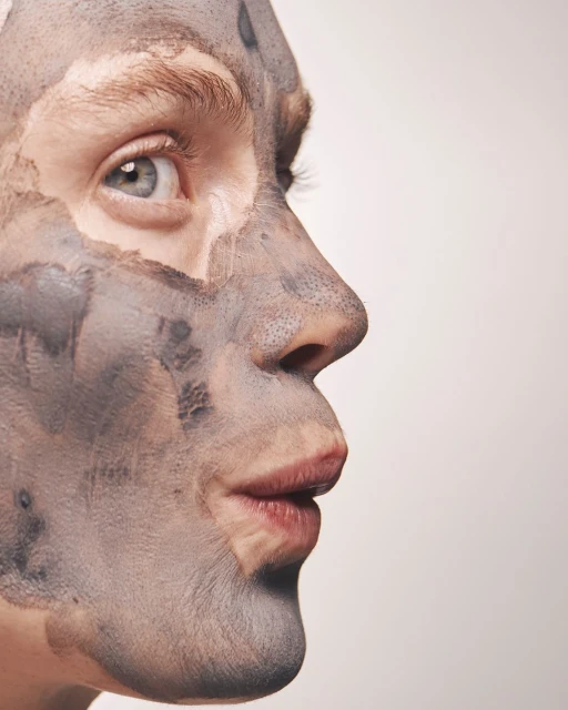 Close-up of a man's face covered in a grey clay mask, side profile, against a neutral background in a beauty concept. Skincare.